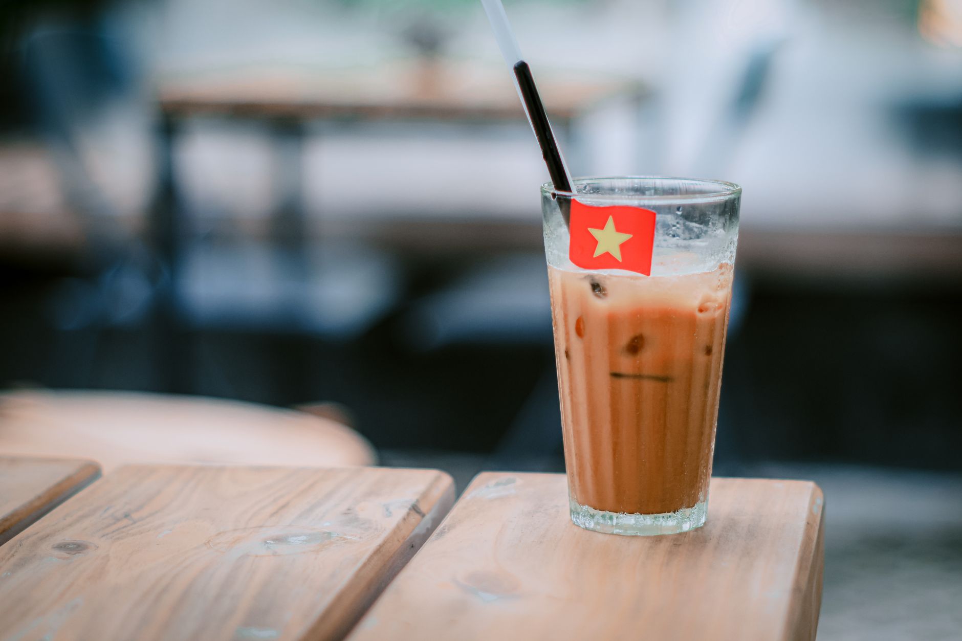 Glass of iced coffee with a Vietnamese flag stirrer on a wooden table.