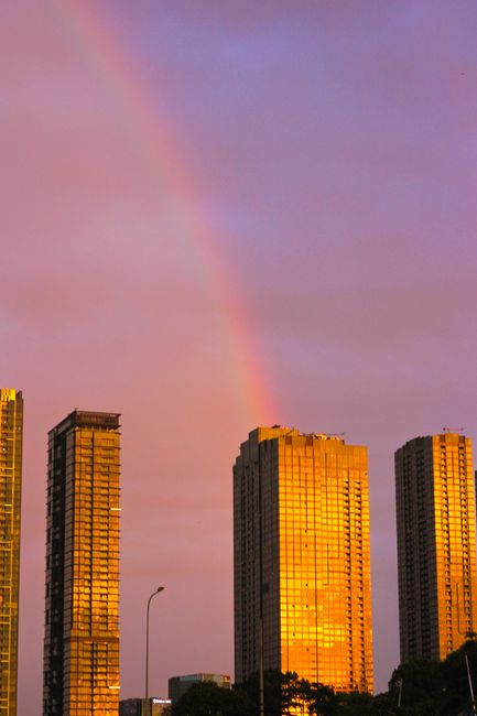 Dramatic sunset over Ho Chi Minh City with a rainbow arching above skyscrapers.