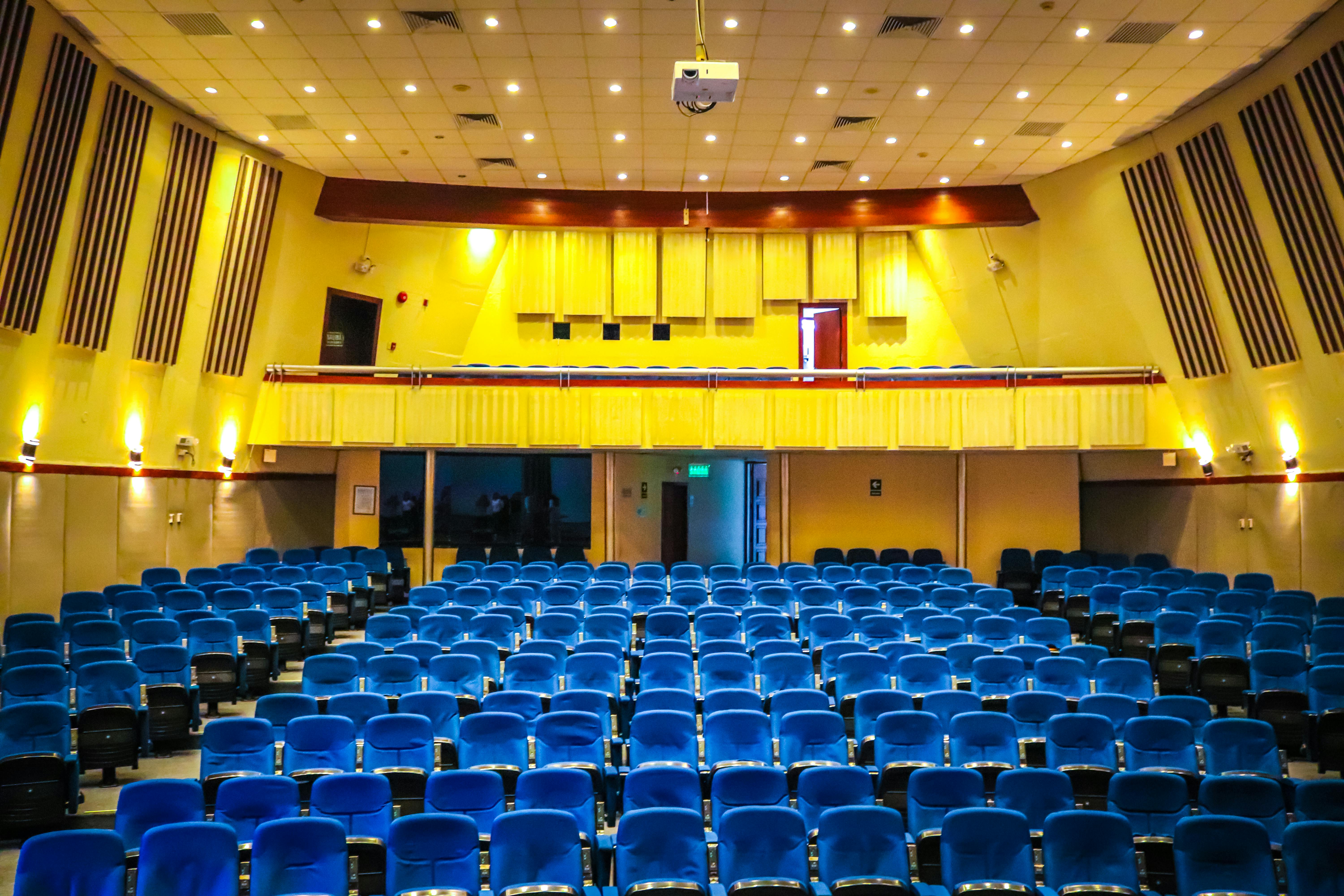 Free Wide-angle view of a vibrant auditorium with blue seats and yellow walls, perfect for events. Stock Photo