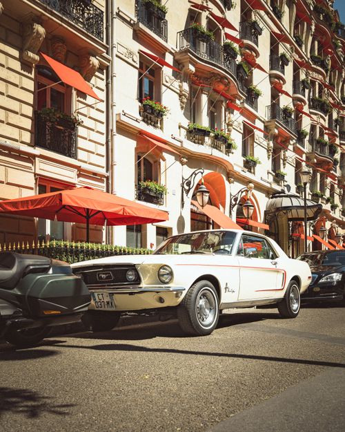 Free Elegant white Ford Mustang parked in front of a historic Parisian building with red accents and balconies. Stock Photo