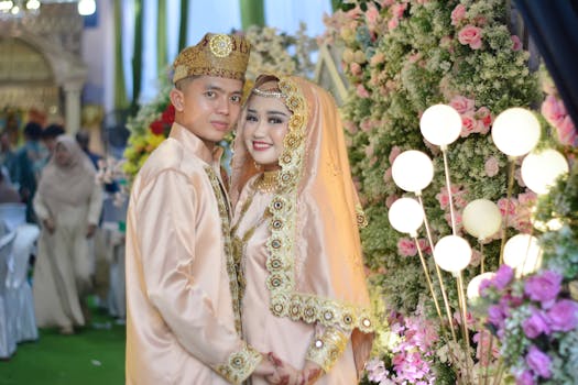 A joyful couple in ornate traditional wedding attire surrounded by floral decorations.