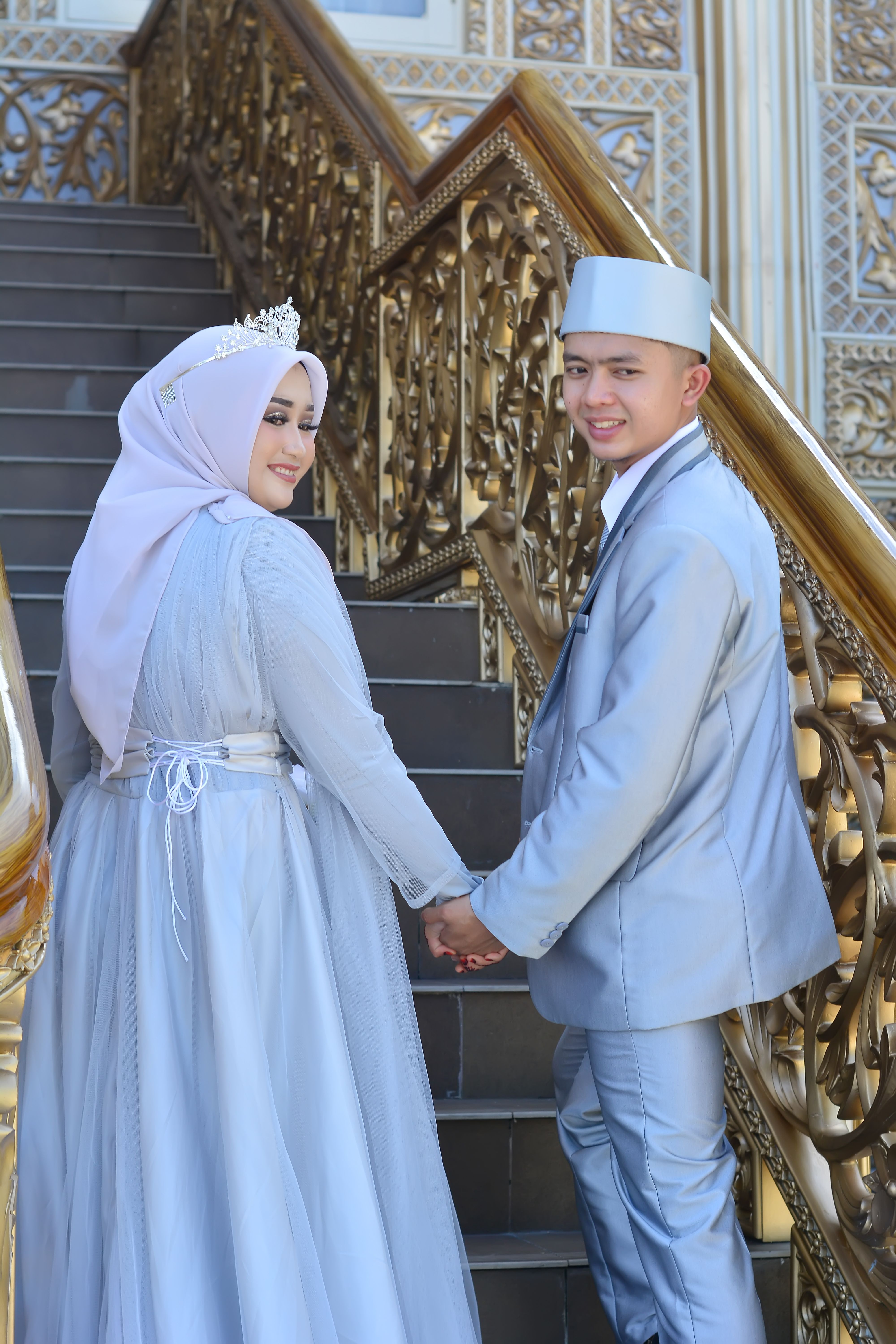 A Muslim bride and groom in traditional attire pose on beautiful staircase.