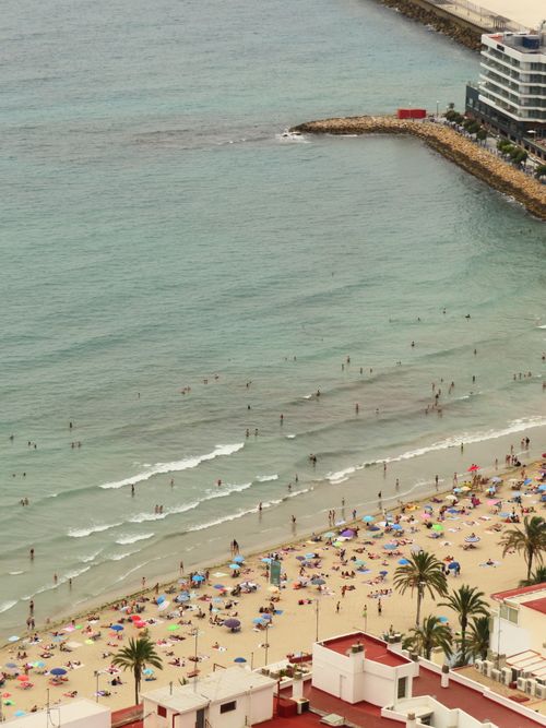 Free Vibrant beach scene with people and colorful umbrellas, viewed from above, showcasing coastal leisure. Stock Photo