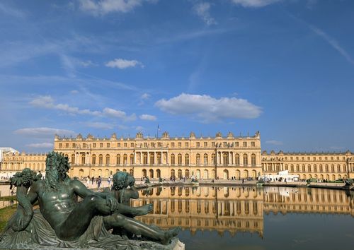 Free Breathtaking view of the Palace of Versailles with sculptures and water reflection under a blue sky. Stock Photo