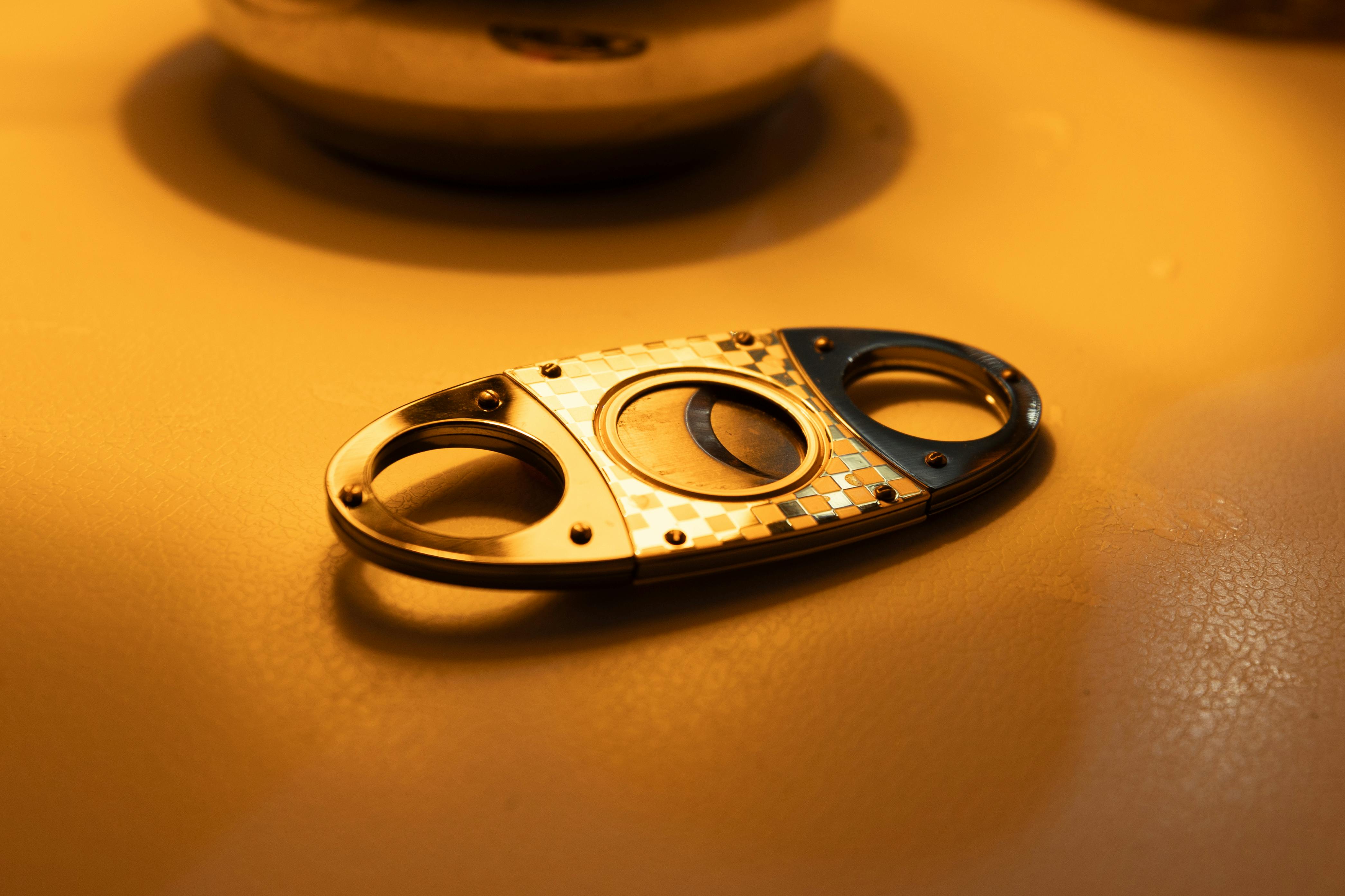 Close-up of a premium double-blade cigar cutter resting on a table under warm lighting.