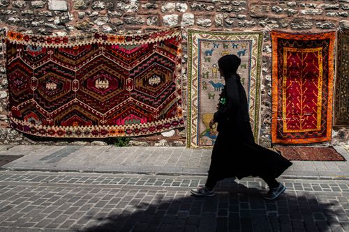 Free A silhouette of a woman walking past vibrant oriental rugs in Istanbul. Stock Photo