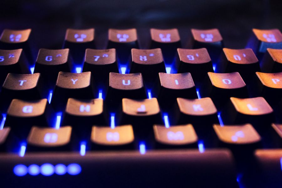 Vibrant close-up of a backlit computer keyboard in a dark setting with glowing blue lights.