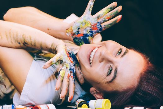 Smiling woman laying surrounded by paint making art with colorful hands.