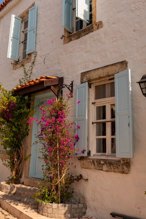 Free Sunlit Mediterranean house facade with blue shutters and bougainvillea. Stock Photo