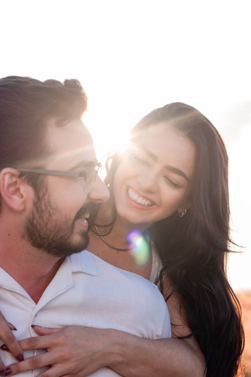 Free Happy couple embracing at sunset, smiling joyfully against a bright sky. Stock Photo