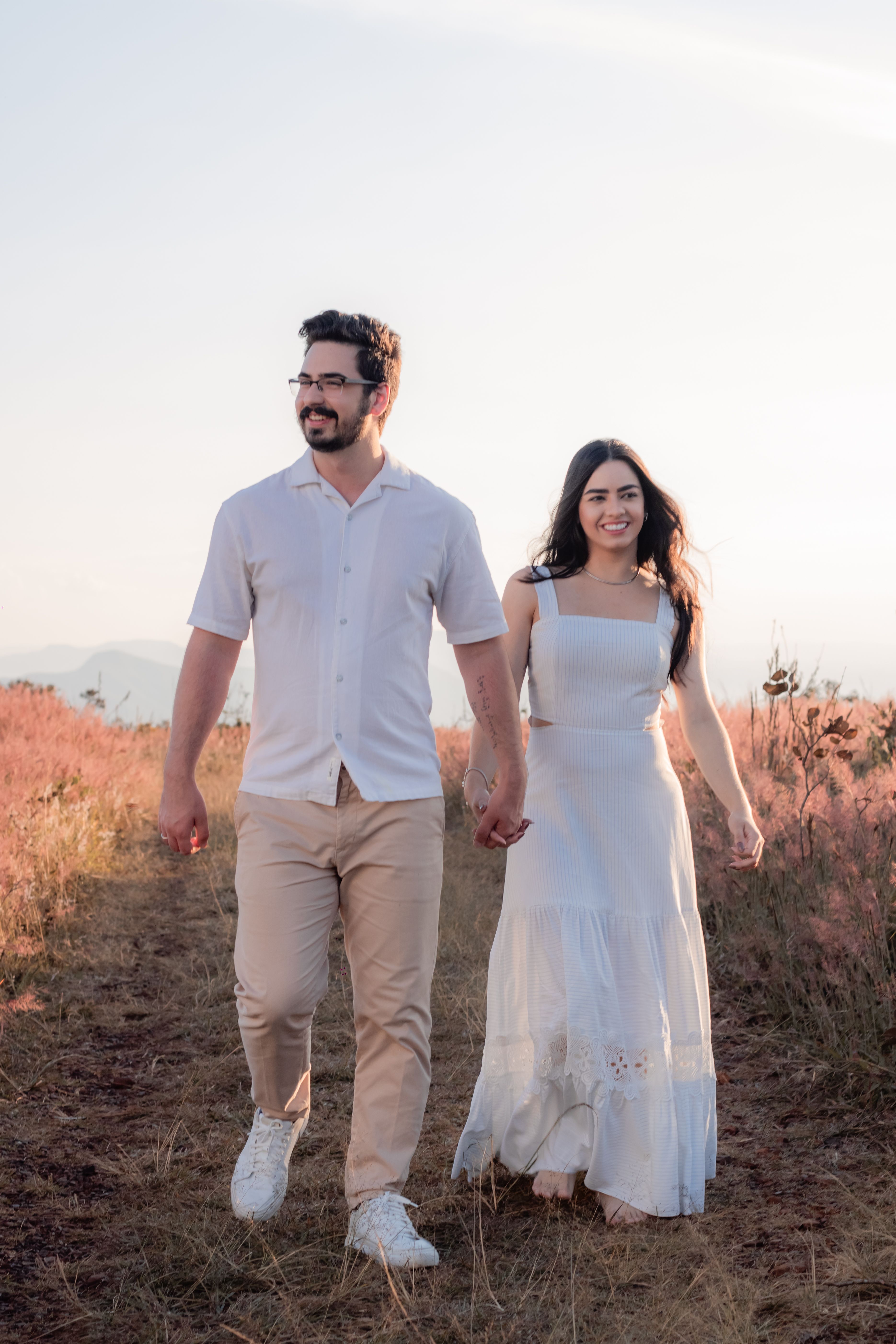 Happy couple walking through a sunny meadow, holding hands, enjoying a romantic moment.