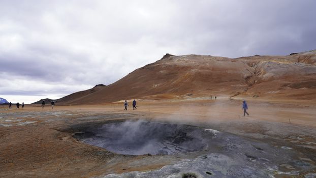 Tourists exploring a geothermal area with steaming hot springs and rugged terrain in Iceland.