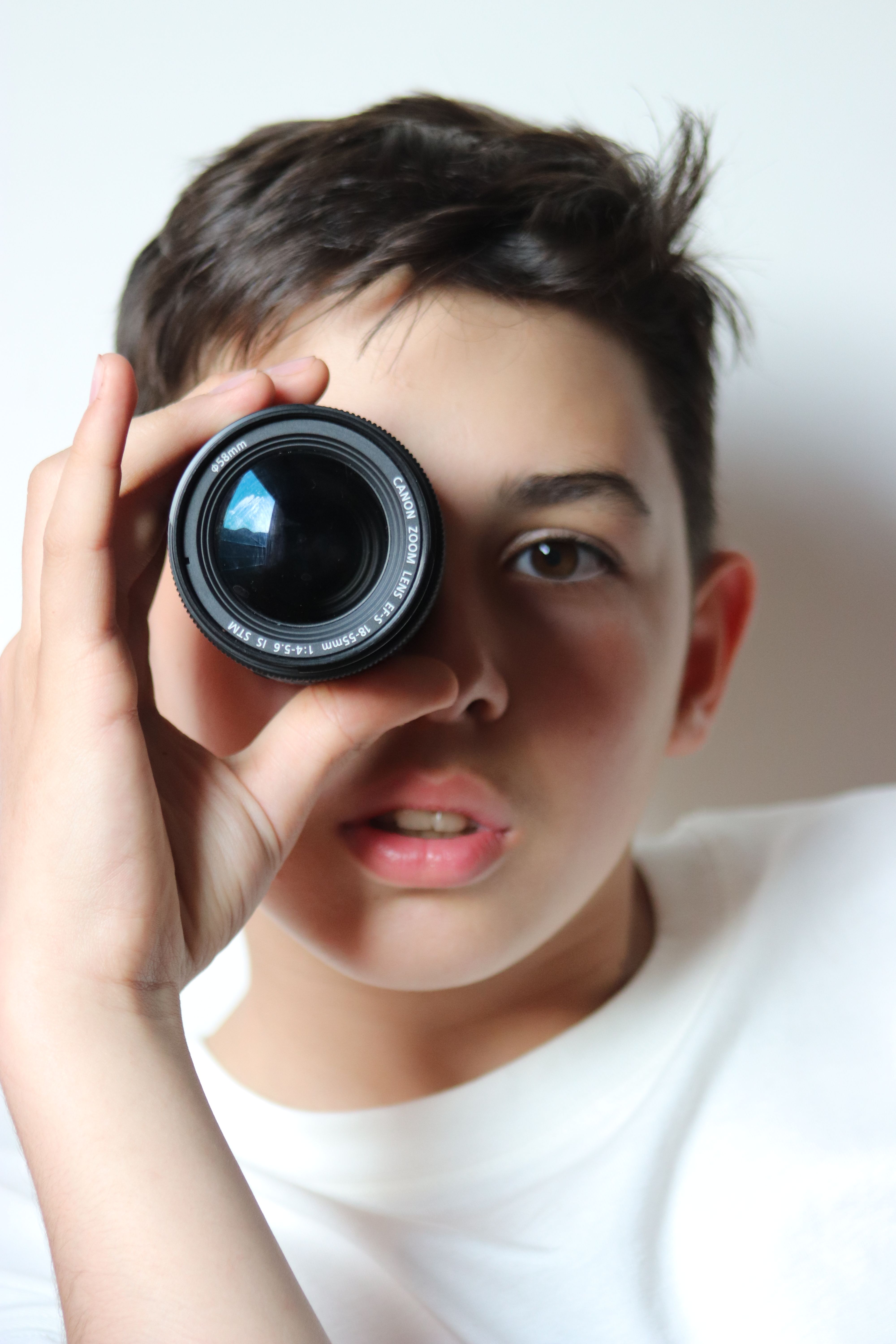 Teen boy peering through a camera lens with curiosity and focus.