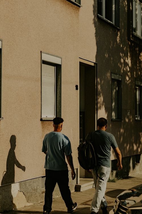Free Two people walking past buildings in Kassel, Germany, during sunset casting long shadows. Stock Photo
