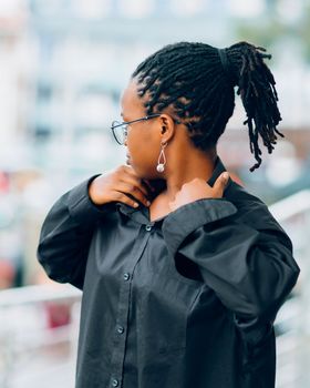 Profile of a woman with dreadlocks, glasses, and earrings wearing a black shirt.