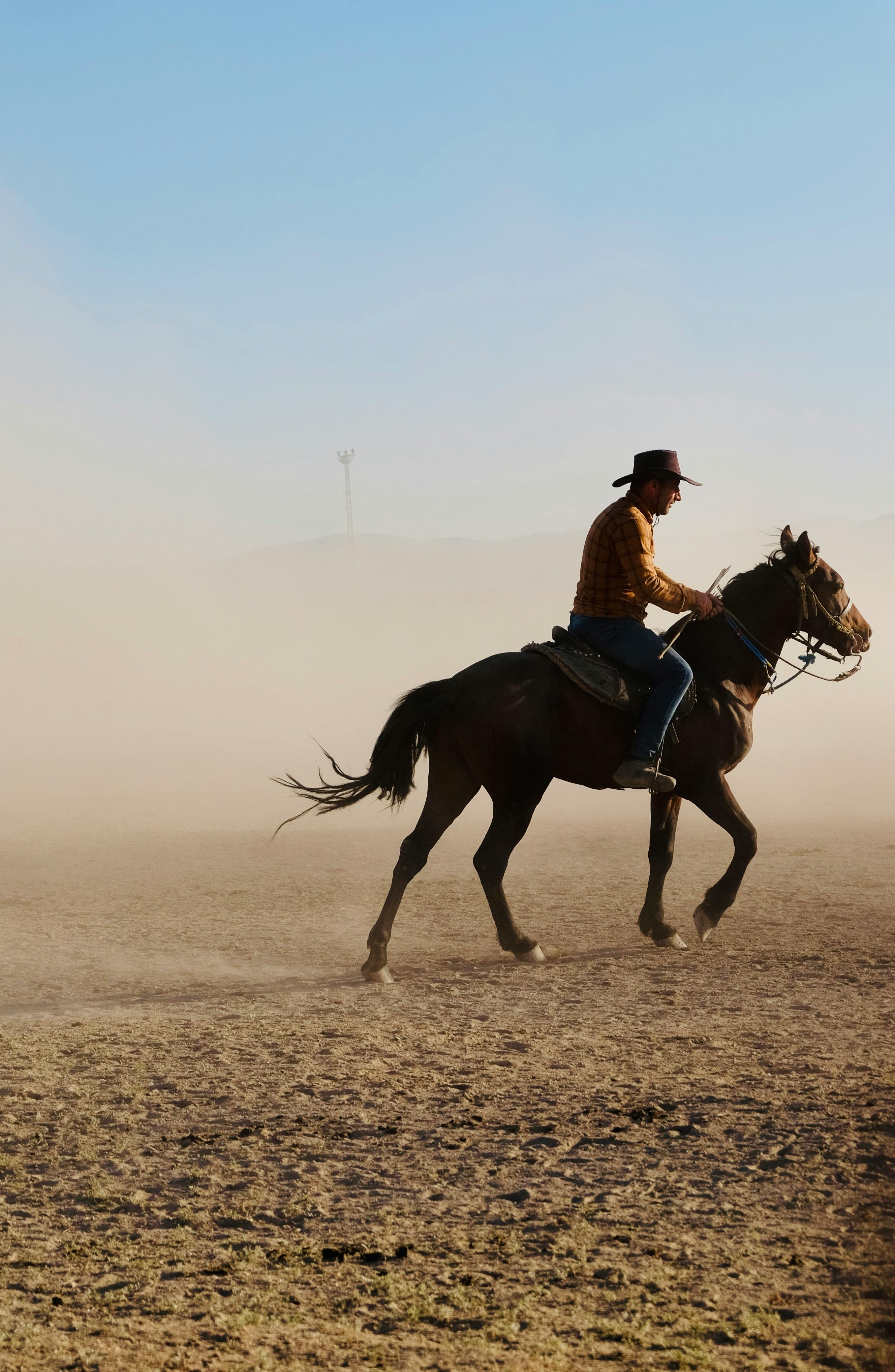 A cowboy riding through a dusty field in Hürmetci, Kayseri, Türkiye, under a clear sky.