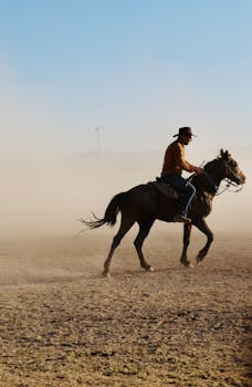A cowboy riding through a dusty field in Hürmetci, Kayseri, Türkiye, under a clear sky.