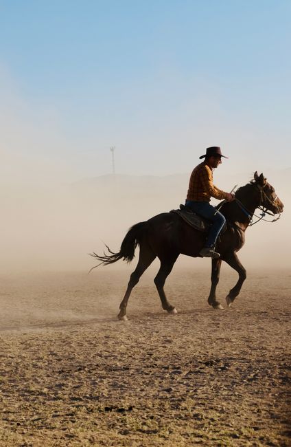 A cowboy riding through a dusty field in Hürmetci, Kayseri, Türkiye, under a clear sky.