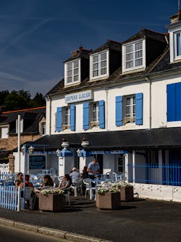 Quaint French creperie with blue shutters and outdoor dining area on a sunny day.