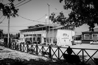 Monochrome image of a rustic building in a quaint urban setting with trees and benches.