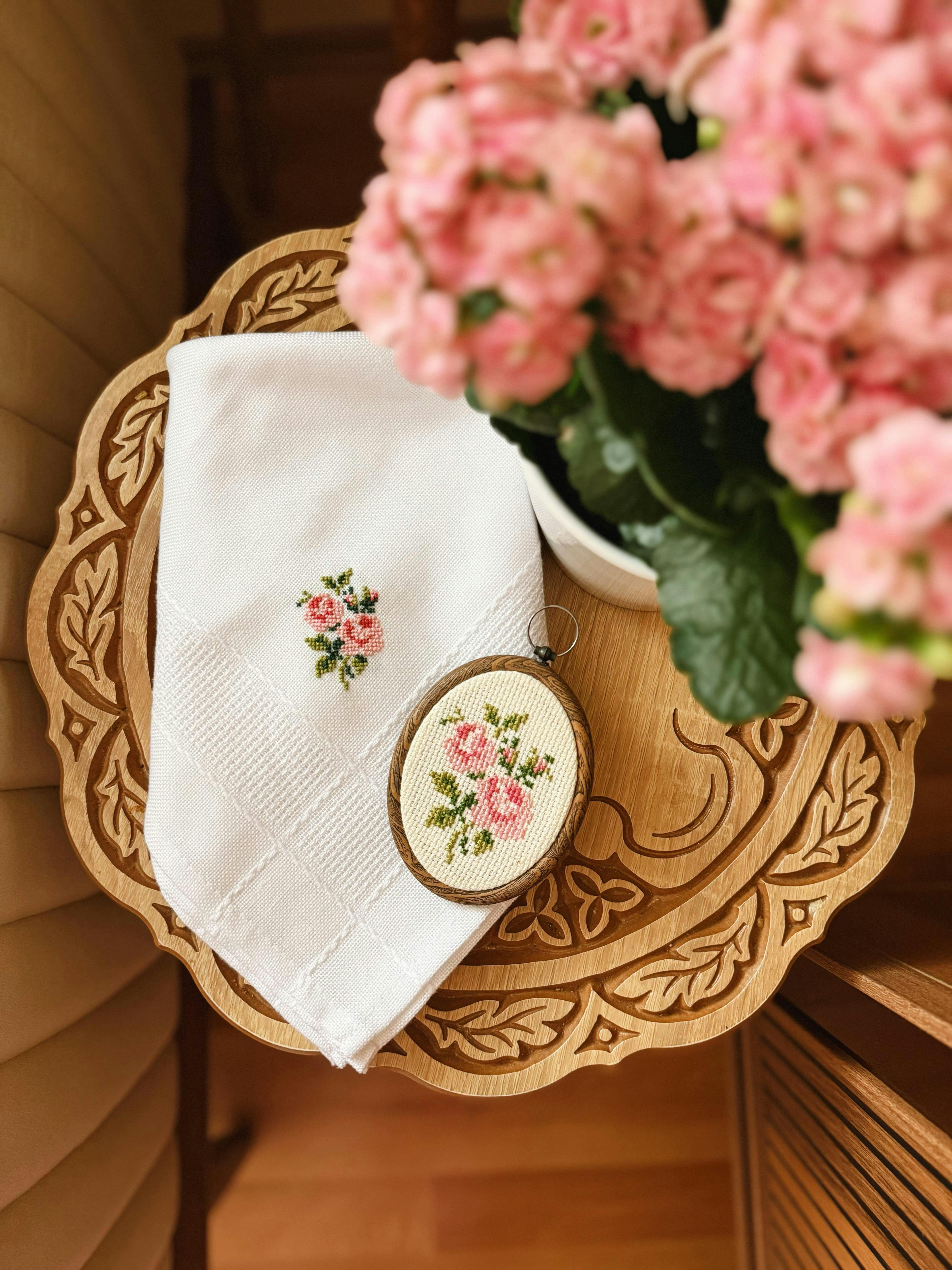 Close-up of rose embroidery and flowers on a carved wooden table.