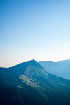 Experience tranquility with a breathtaking aerial view of a mountain ridge at sunrise, under clear blue skies.