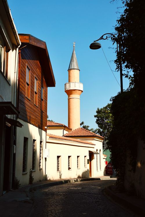 Free Charming view of a narrow alleyway featuring a historic mosque minaret under a blue sky. Stock Photo