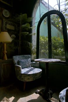 Charming vintage-themed cafe corner with armchair and table by arched window with natural light.