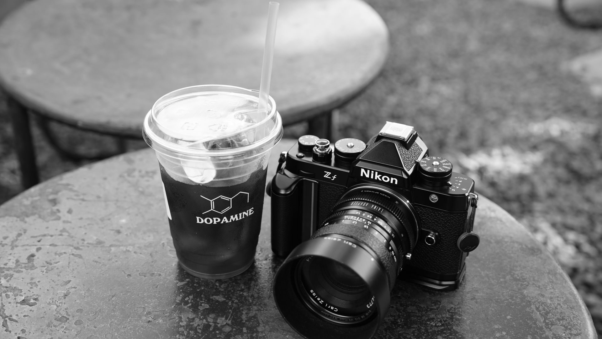 Modafinil and Dopamine: Unlocking the Brain's Secrets Black and white photo of a vintage camera beside iced coffee on a round outdoor table.