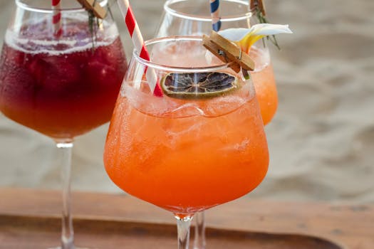 Close-up of vibrant summer cocktails with straws on a wooden tray at the beach.