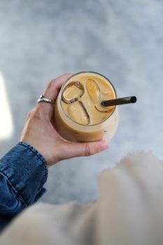 A close-up of a person's hand holding an iced coffee with a straw, capturing the cool and refreshing beverage.