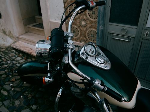 Free A classic motorcycle parked outdoor on a cobblestone street beside a building. Stock Photo