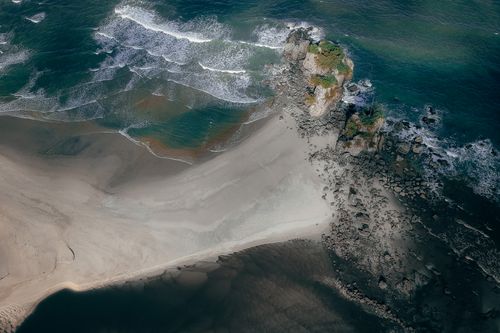 Free Stunning aerial view of a rocky coastline meeting serene ocean waves. Ideal for nature lovers. Stock Photo