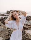 日落时分，一位身穿白色连衣裙的时尚女子在岩石海滩的海边摆姿势