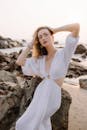 日落时分，身着白色连衣裙的优雅女子在岩石海滩上摆姿势