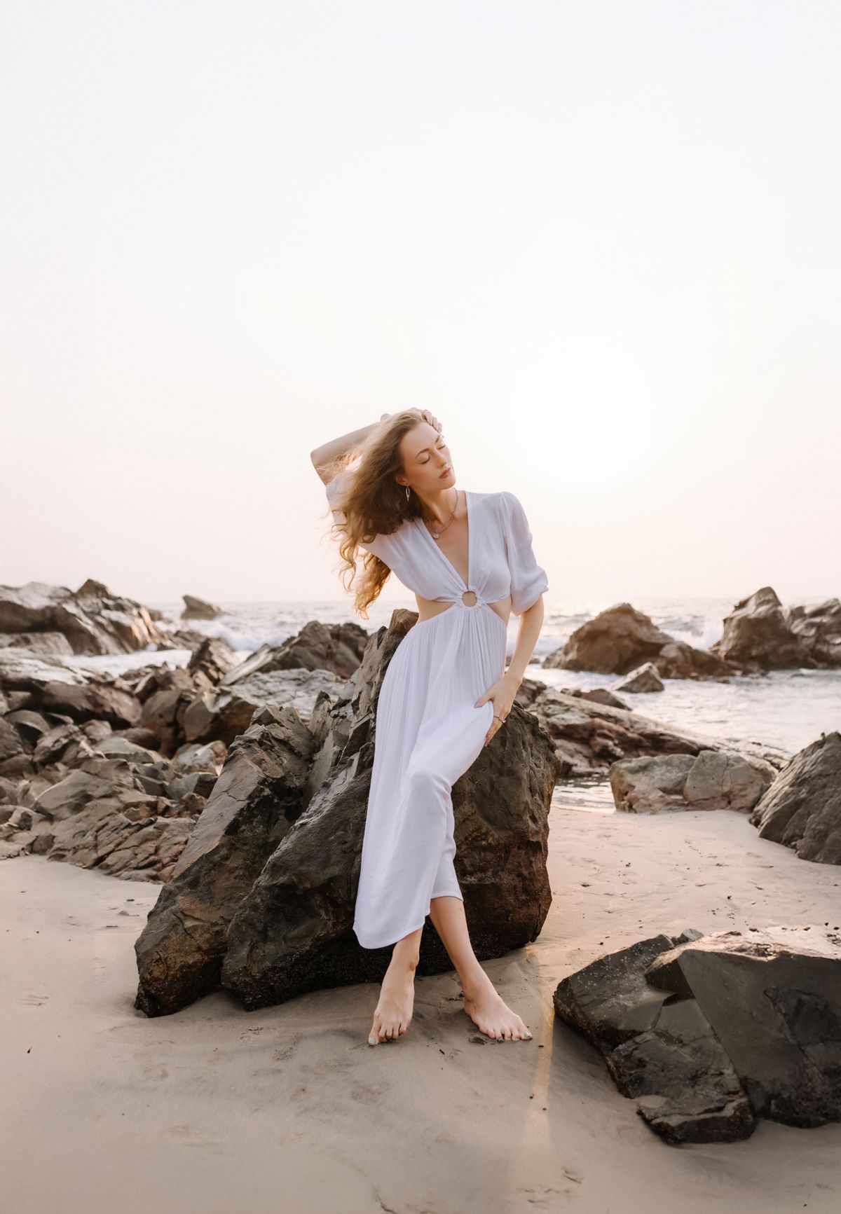 An elegant woman in a white dress on a rocky beach, the white kaftan at its most timeless