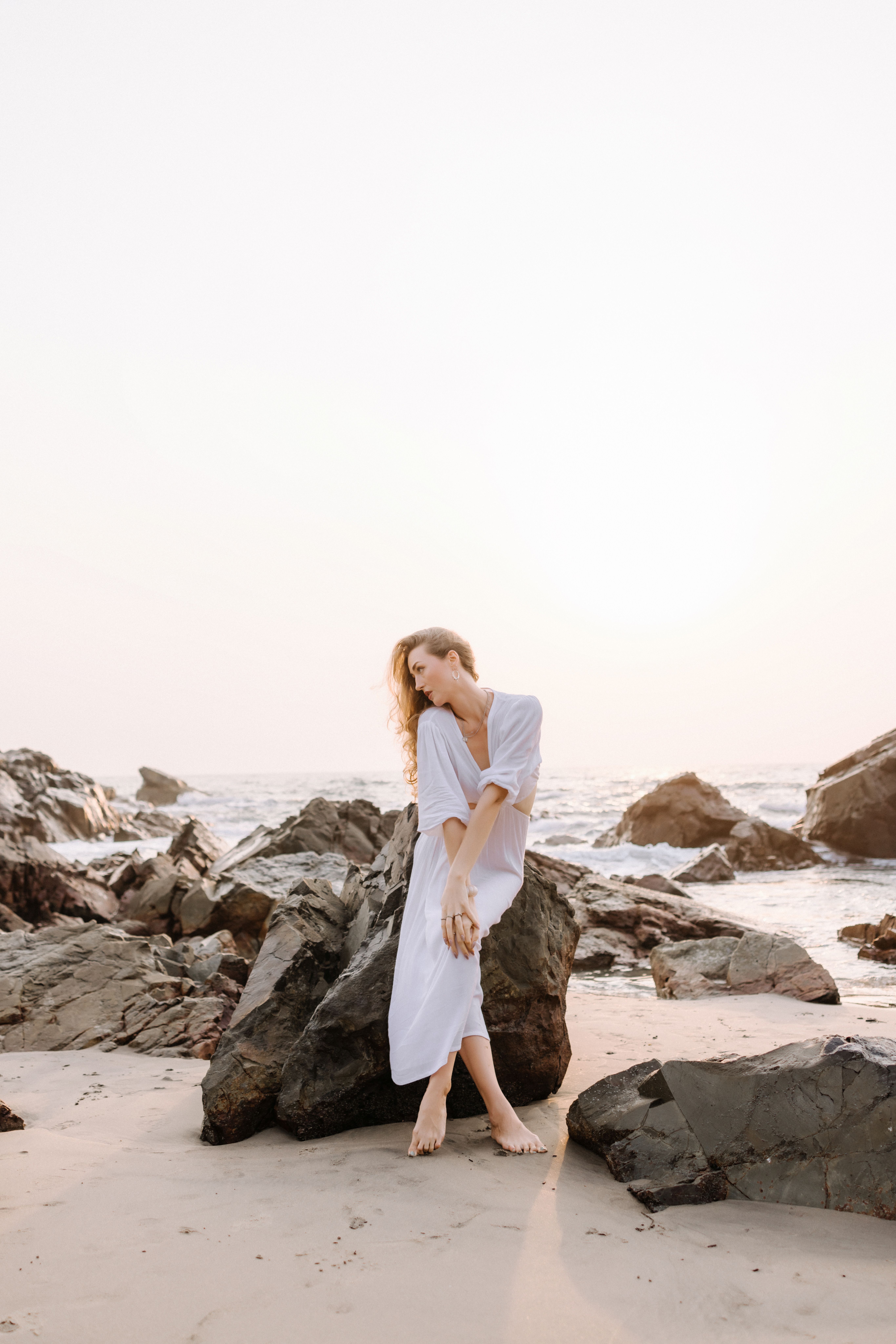 Woman in White Dress Posing on Rocky Beach at Sunset · Free Stock Photo