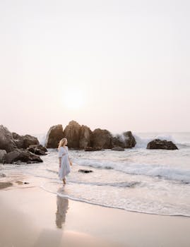 A serene scene of a woman walking along a rocky beach at sunrise.