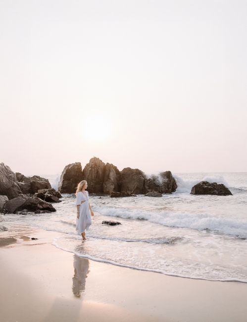 A serene scene of a woman walking along a rocky beach at sunrise.