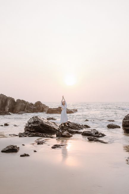 Person meditating on rocky beach during sunset, creating a calm and serene atmosphere.