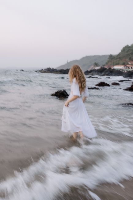 Blurry image of a woman in white dress walking along the ocean shore at twilight.