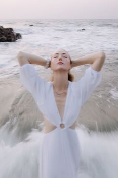 A woman in a white dress enjoys the ocean breeze, standing in gentle waves.