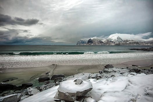 Snow-covered beach and mountains in Lofoten, Norway, under dramatic skies.