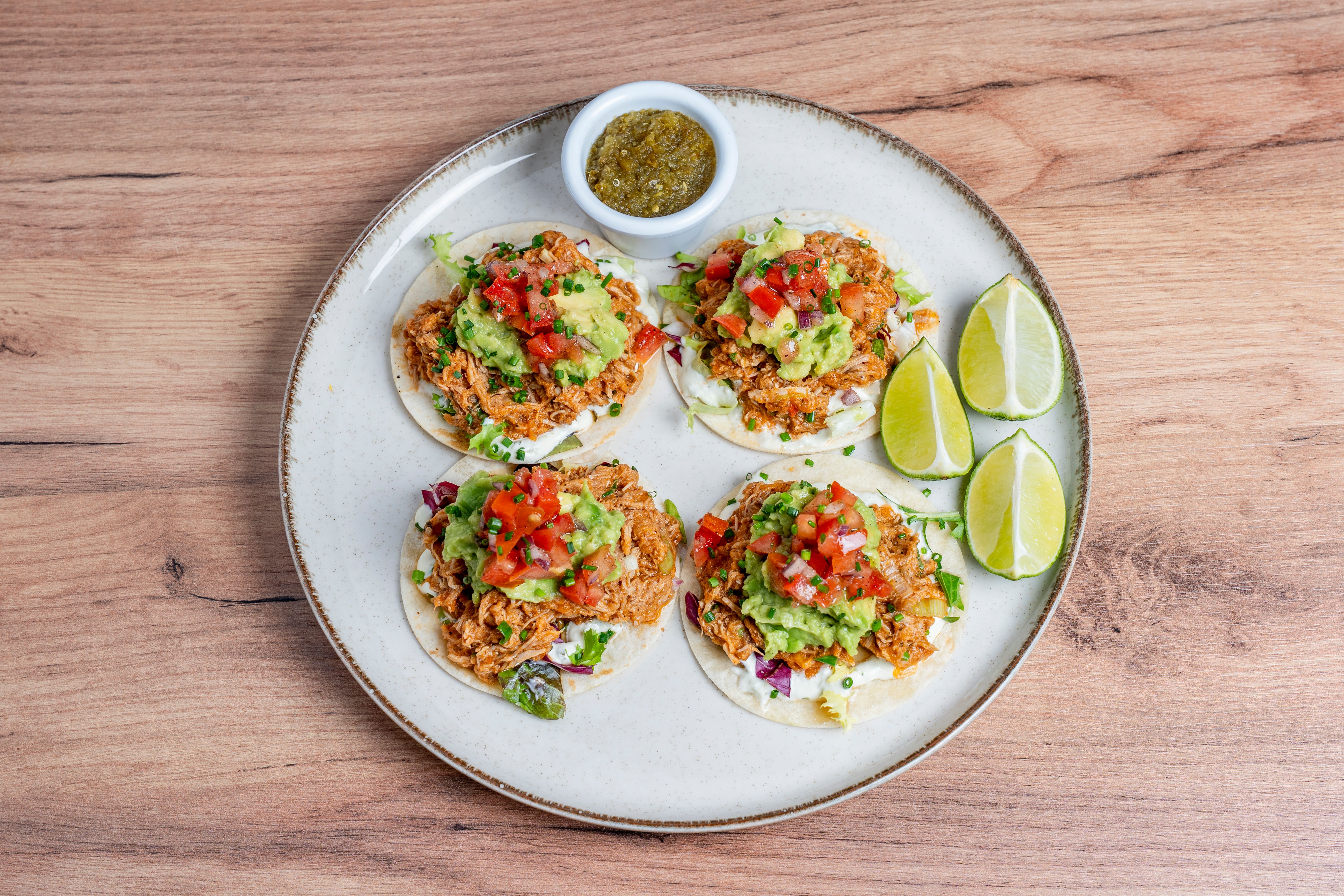 A generous portion of glossy, mahogany-colored shredded chicken tinga on a white plate, garnished with bright white diced onions and fresh green cilantro