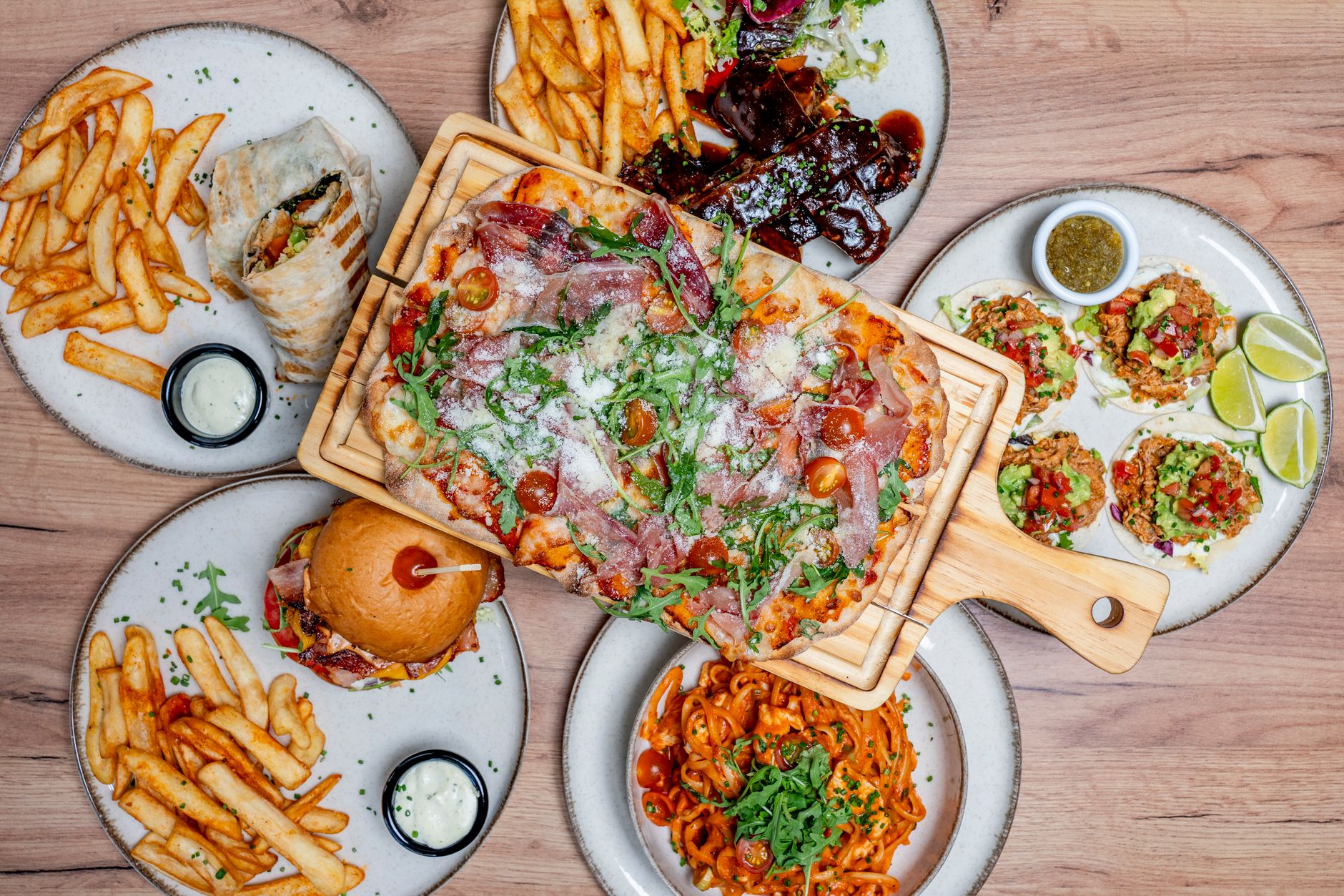 Top view of a diverse spread of Mediterranean dishes including pizza, pasta, and wraps.