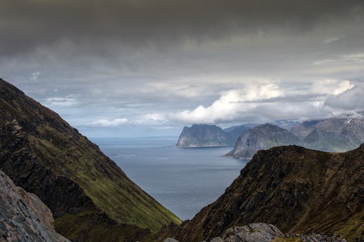 A stunning view of the Lofoten fjord surrounded by rocky mountains and a dramatic cloudy sky.