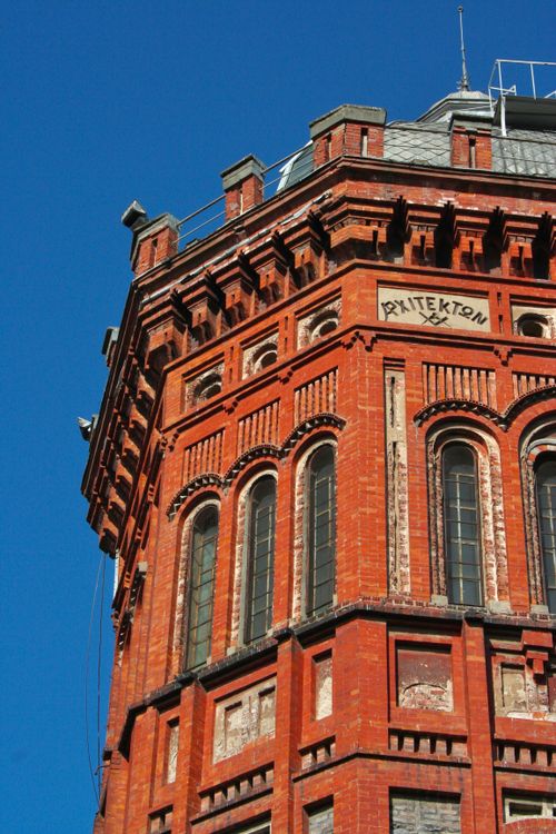 Free A detailed view of a historic red brick tower with tall arched windows under a clear blue sky. Stock Photo