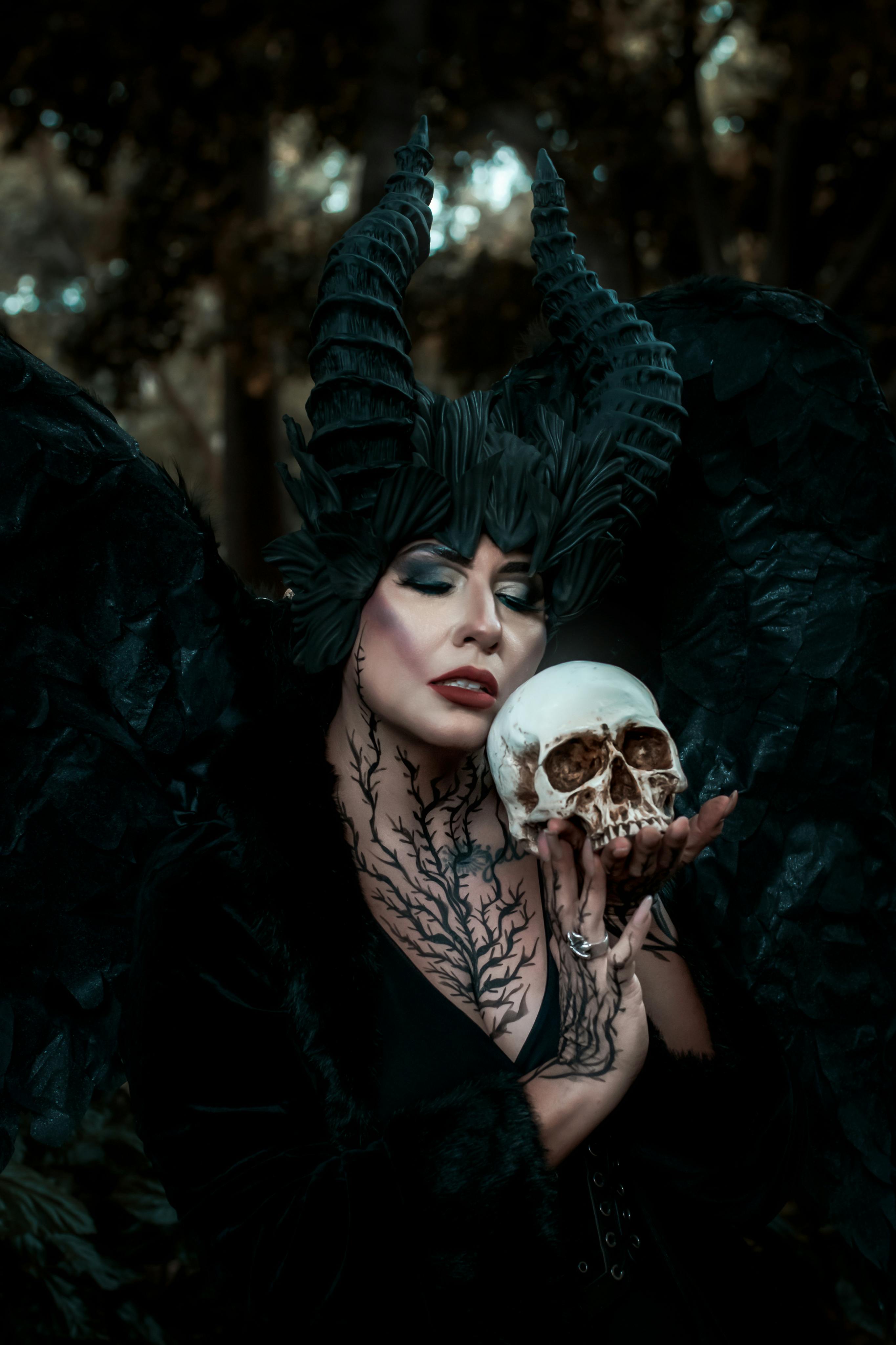 grátis Figura misteriosa em traje escuro com chifres segura uma caveira em um cenário de floresta fantástica. Foto profissional