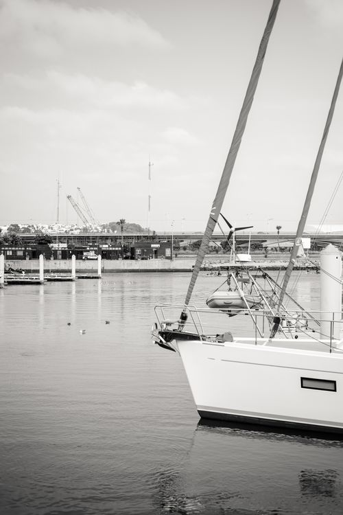 Free Black and white photo of a sailboat docked in Rabat's marina, reflecting on calm waters. Stock Photo