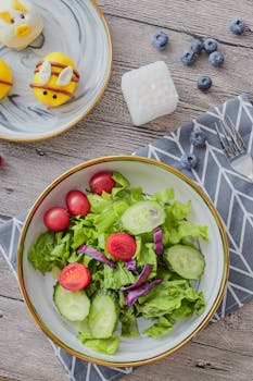 Overhead view of fresh vegetable salad with fun fruit design on a wooden table.